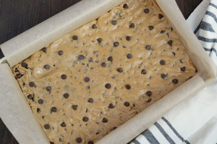 cookie bar dough in a 9 x 13 metal baking pan with parchment paper 