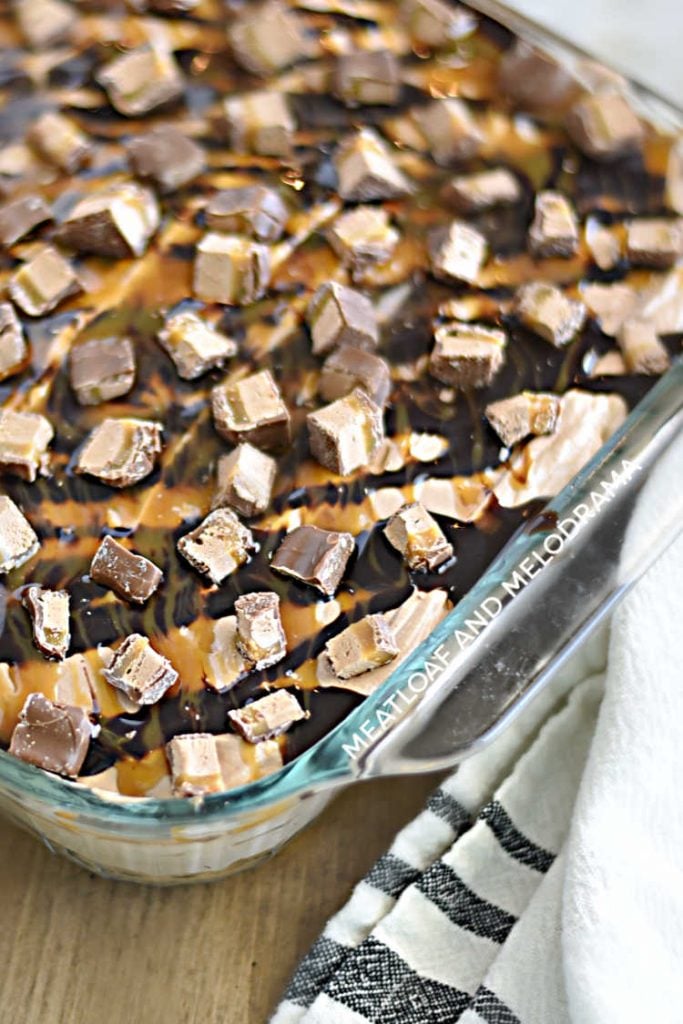 chocolate poke cake with fluffy frosting and milky way candies with chocolate and caramel syrup in a glass pan