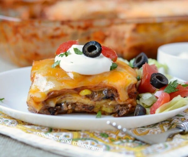 southwestern lasagna enchilada casserole on plate with sour cream lettuce tomatoes and olives