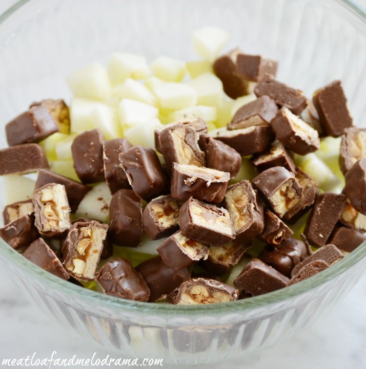diced green granny smith apples and snickers candy bars in a glass mixing bowl