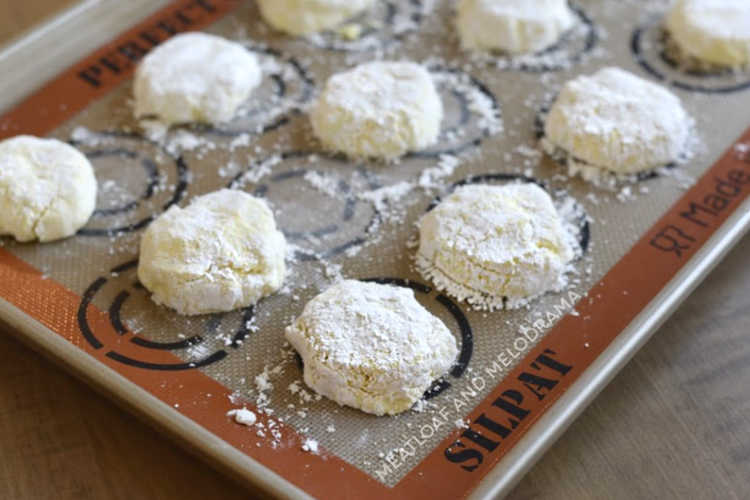 lemon crinkle cookies in powdered sugar on a baking sheet lined with baking mat Silpat