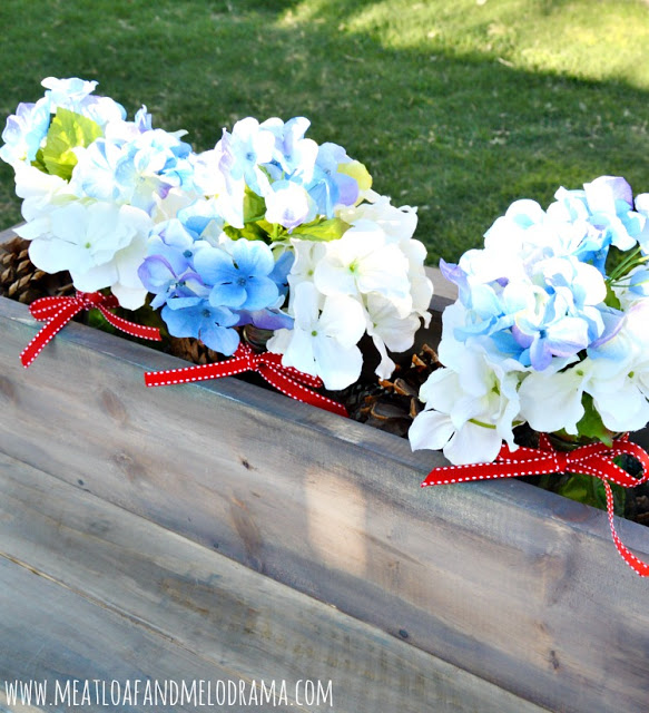 DIY wood planter box centerpiece filled with flowers and pinecones for 4th of July