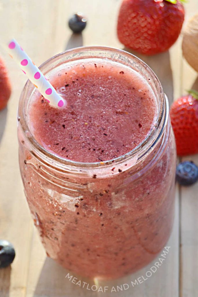 close up of dark pink, mixed berry fruit smoothie in a mason jar with straw