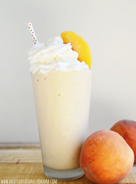 peach milkshake in a tall glass with fresh peaches