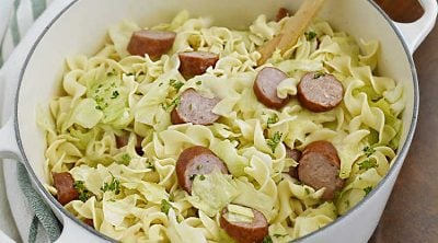 haluski and kielbasa, fried cabbage with noodles and smoked sausage in a white dutch oven