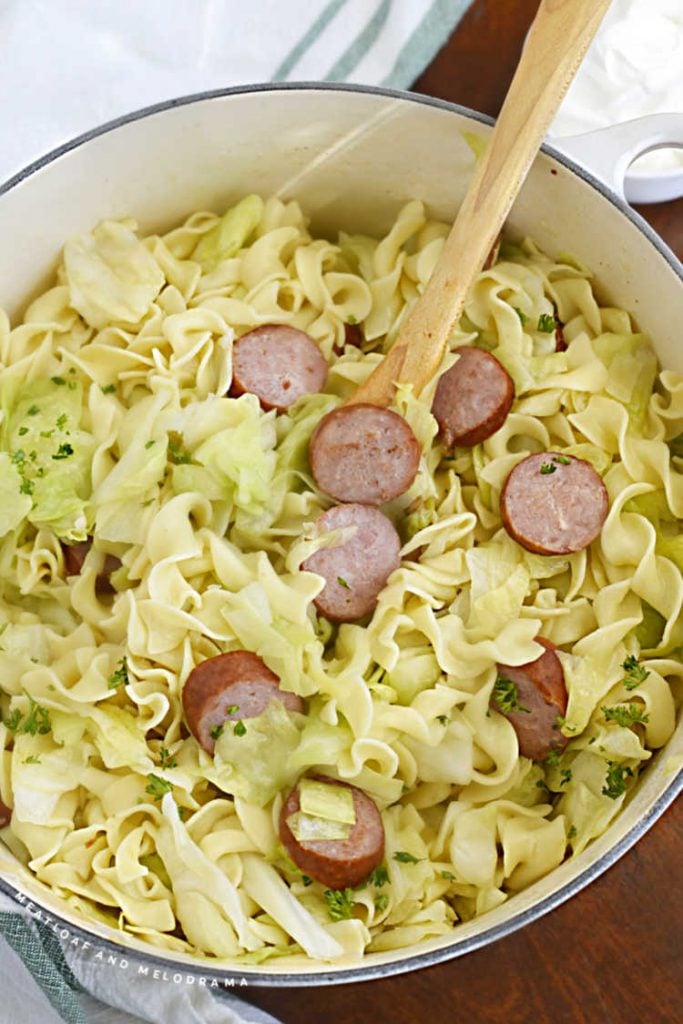 cabbage, noodles and kielbasa with wooden spoon in a dutch oven