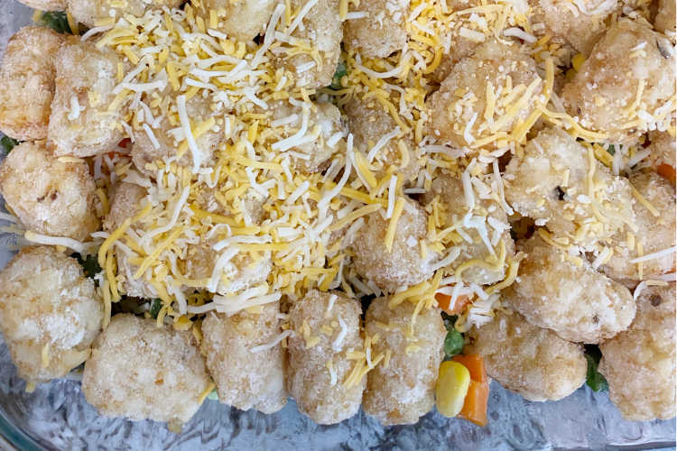 frozen tater tots over ground beef and vegetables in a baking dish