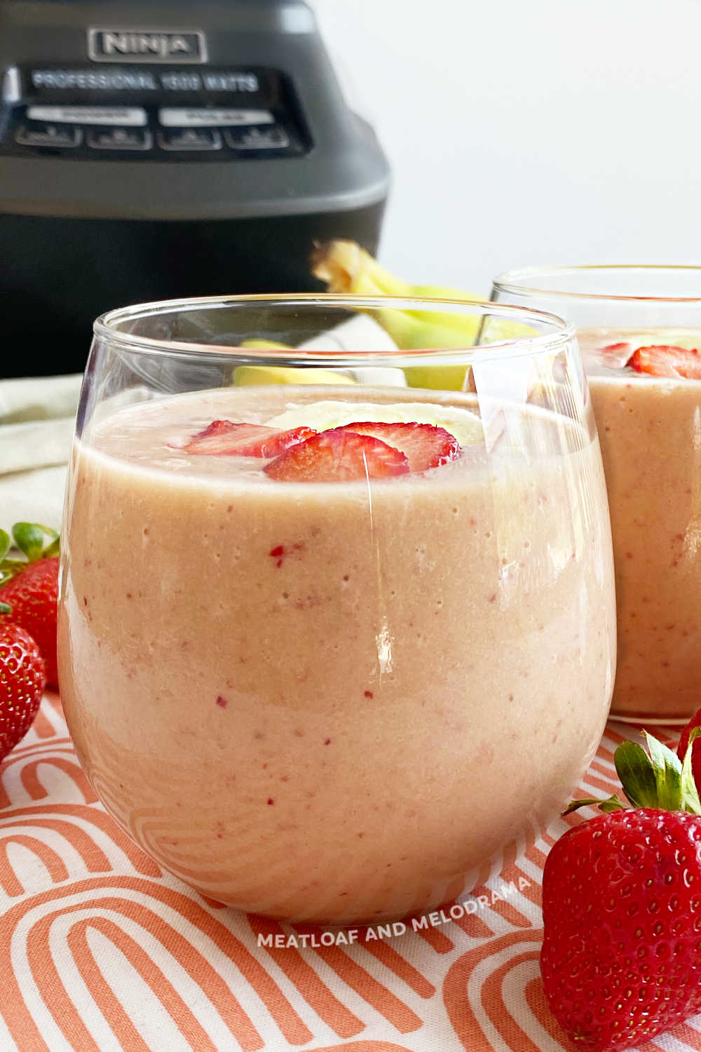 strawberry banana breakfast smoothie with protein powder in glass in front of ninja blender