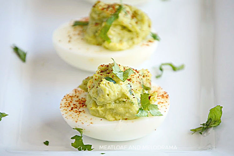guacamole deviled eggs with mashed avocado and chipotle powder on a white tray