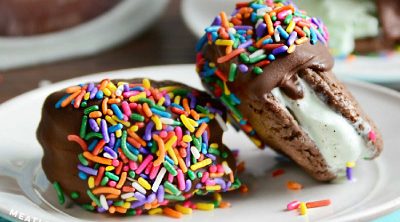 mint chocolate chip cookie ice cream sandwiches dipped in chocolate with sprinkles on plate