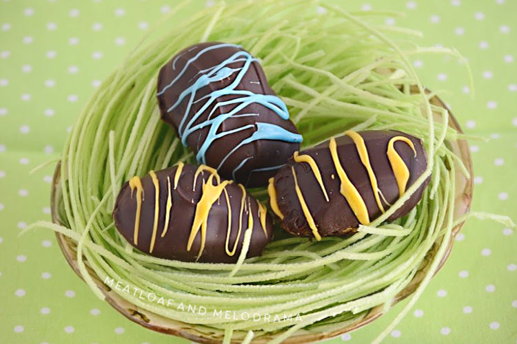chocolate covered peanut butter eggs with yellow and blue stripes in a bowl with edible Easter grass