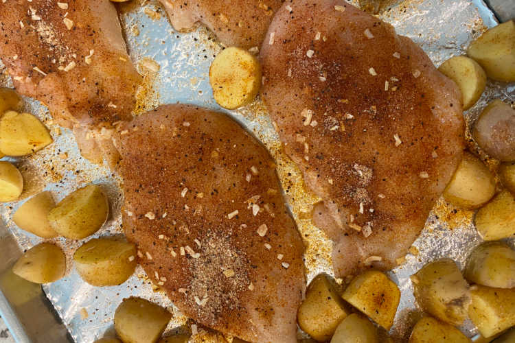 seasoned chicken breasts with potatoes on a baking sheet