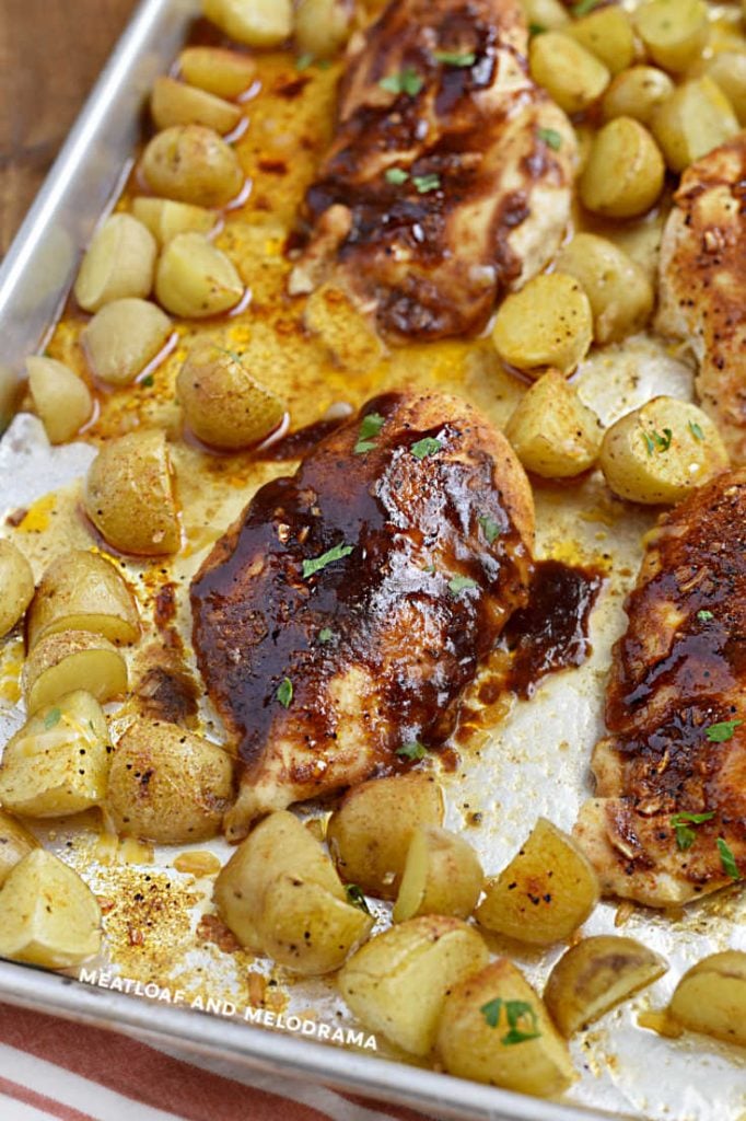 baked chicken breasts with bbq sauce and baby potatoes on a baking sheet