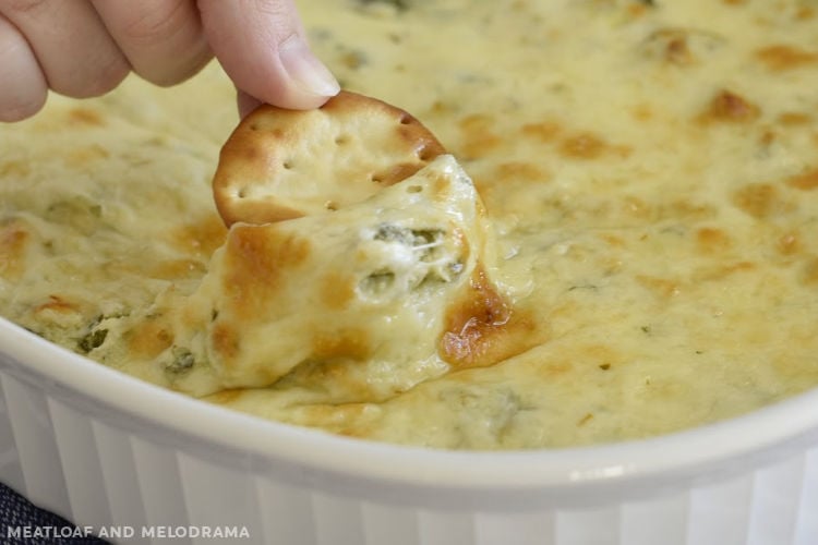 Cheesy warm spinach dip with melted cheese on a cracker
