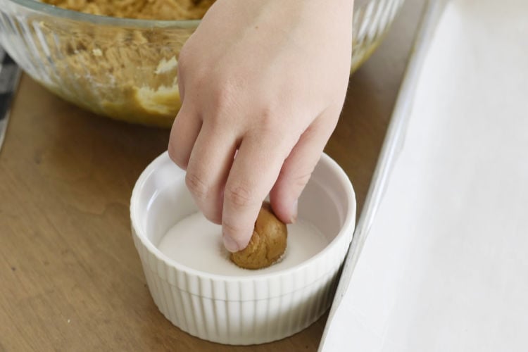 drop molasses cookie dough into white sugar