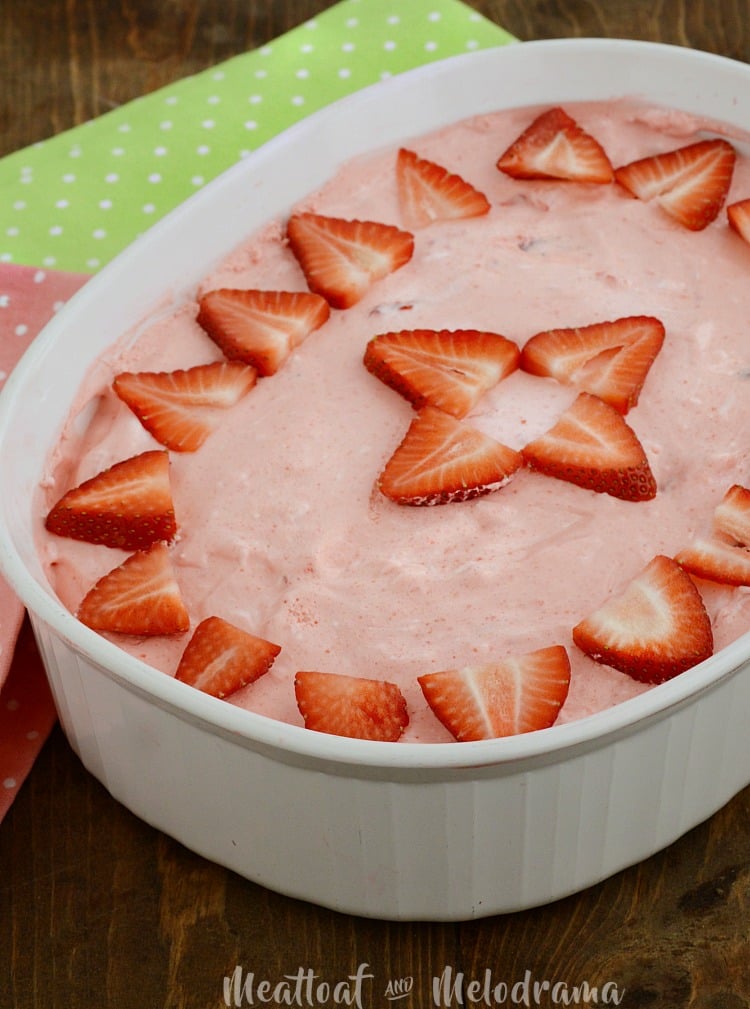 strawberry jello salad topped with strawberries in a white casserole dish