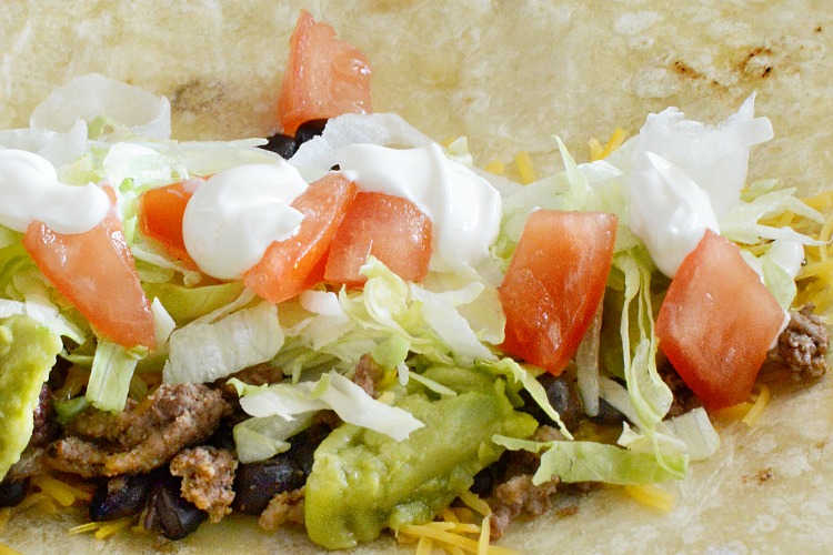 ground beef with lettuce, tomatoes, cheese and sour cream in a tortilla