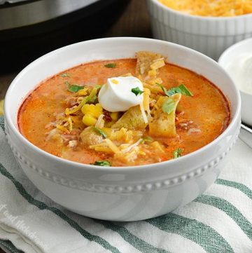 instant pot chicken enchilada soup in white bowl with sour cream, corn chips and cheese