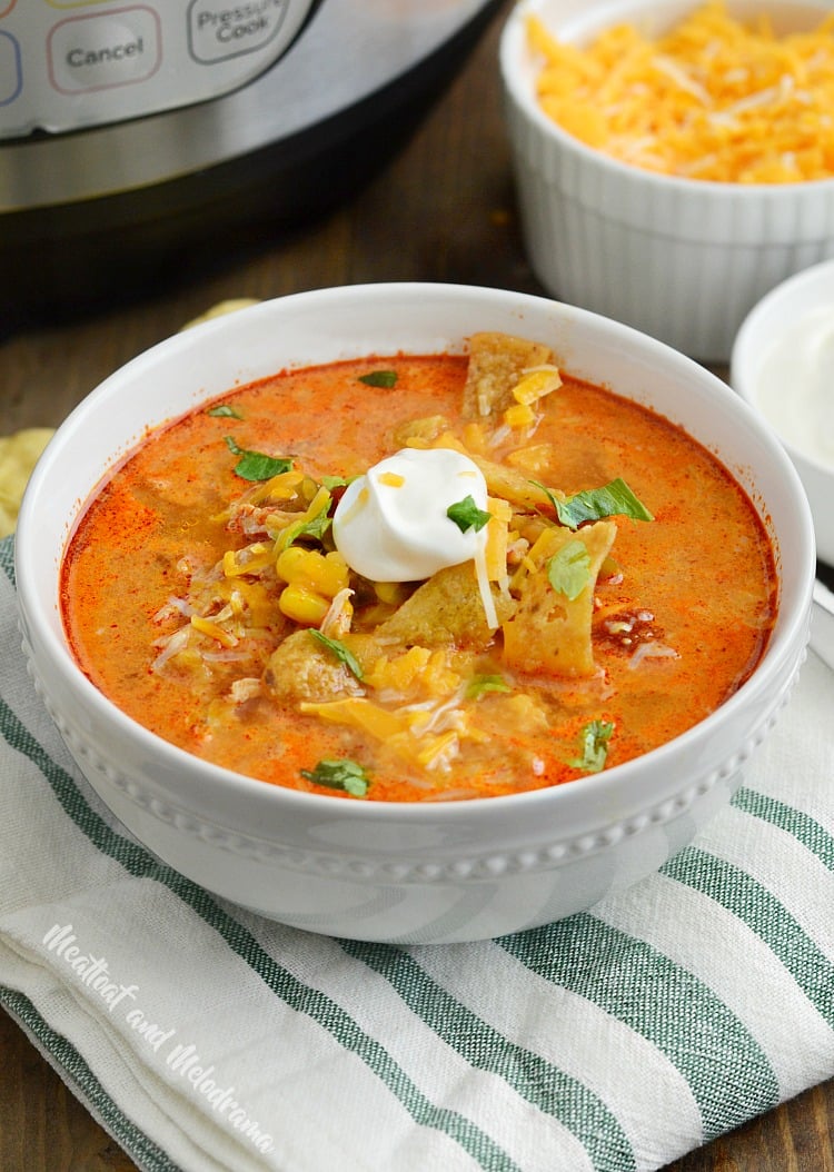 instant pot chicken enchilada soup in bowl topped with corn chips and sour cream and cheese