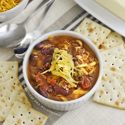 bowl of instant pot chili in white bowl with cheese and saltine crackers