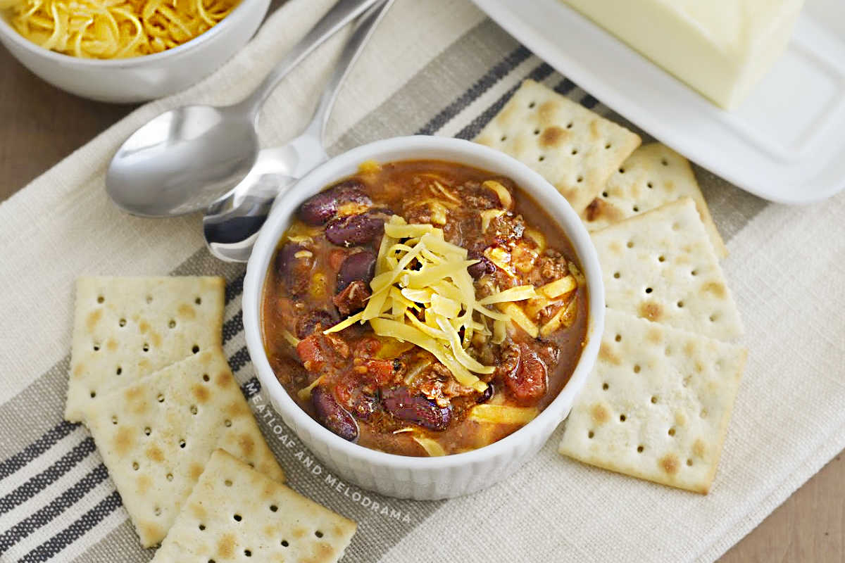 bowl of instant pot chili in white bowl with cheese and saltine crackers