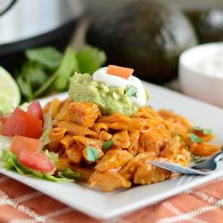 instant pot chicken enchilada pasta on white plate with guacamole, sour cream, tomatoes