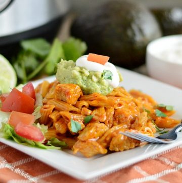 instant pot chicken enchilada pasta on white plate with guacamole, sour cream, tomatoes