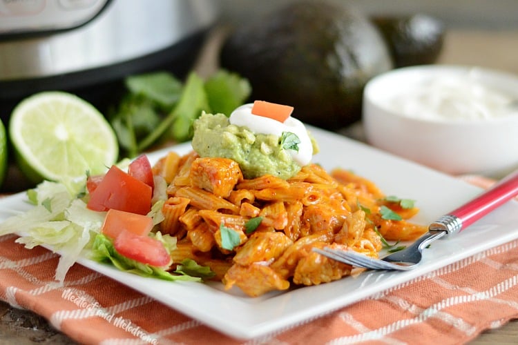 instant pot chicken enchilada pasta on white plate with guacamole, sour cream, tomatoes