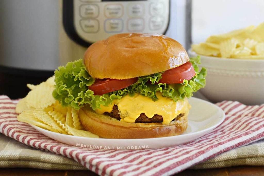 instant pot hamburger with melted cheese, lettuce and tomato slices on a bun with chips