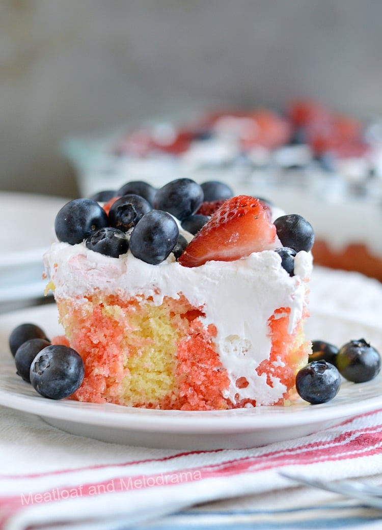 red white and blue poke cake topped with whipped topping and strawberries and blueberries on plate, 