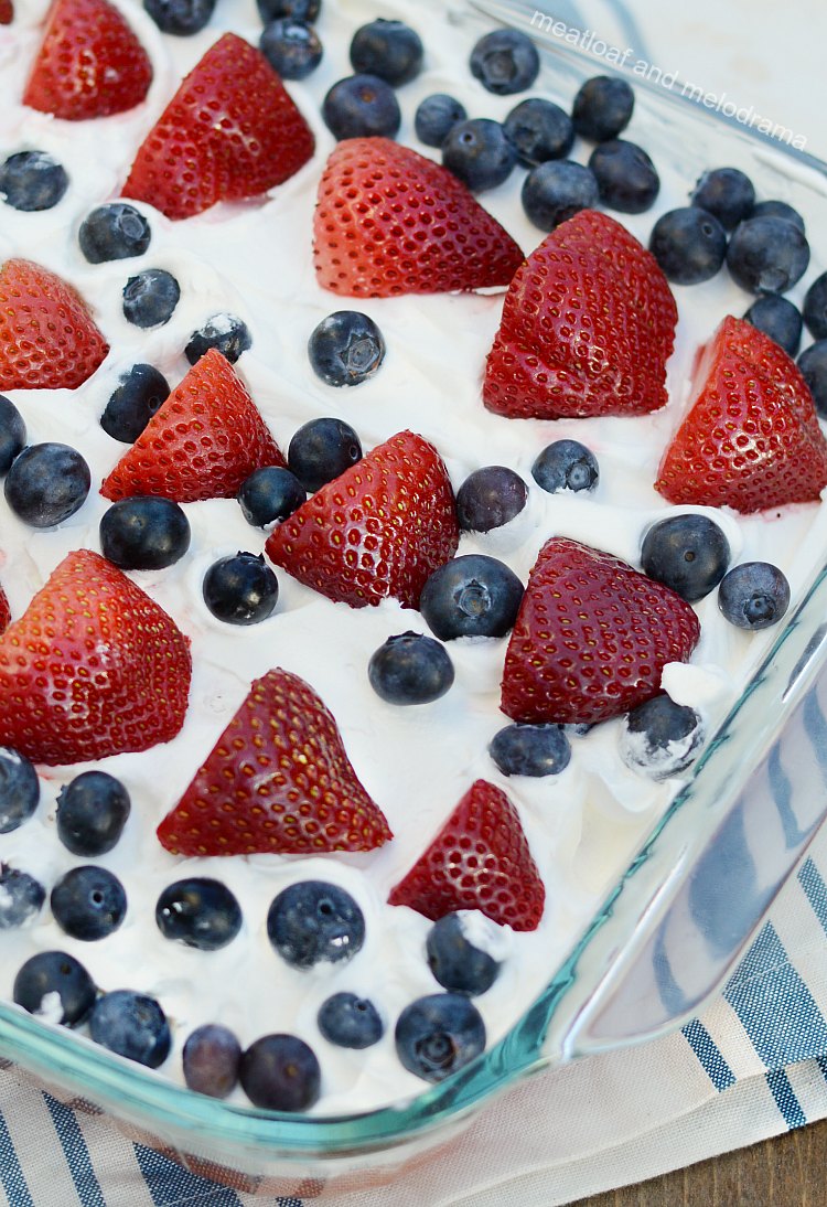 red white and blue poke cake with strawberries and blueberries on whipped topping