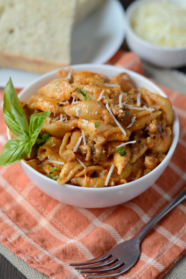 instant pot creamy sausage and shells in white bowl with bread and cheese and basil