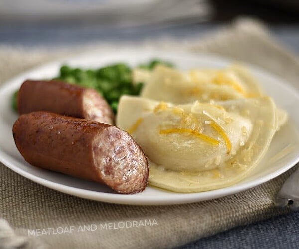 baked pierogies and kielbasa sausage on white plate with peas