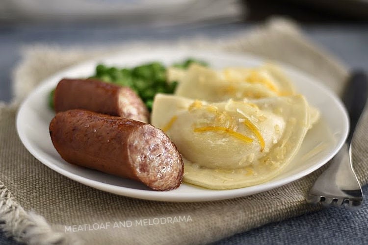baked pierogies and kielbasa sausage on white plate with peas