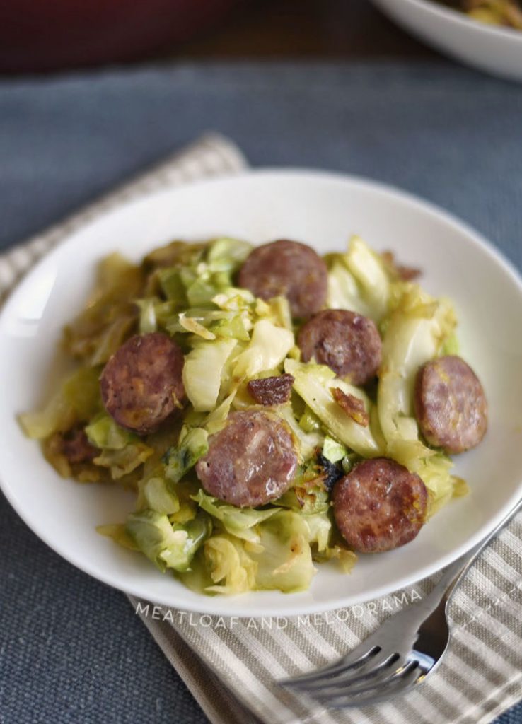 fried kielbasa and cabbage with onions and bacon on white plate