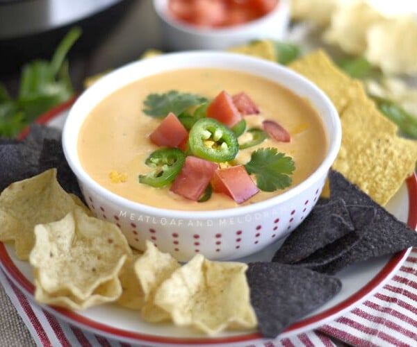 instant pot queso dip in a bowl with tortilla chips and tomatoes and jalapeno peppers