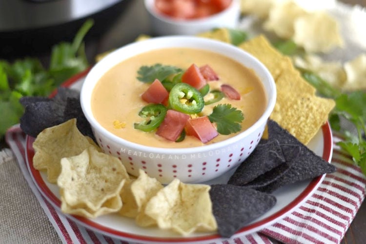 instant pot queso dip in a bowl with tortilla chips and tomatoes and jalapeno peppers