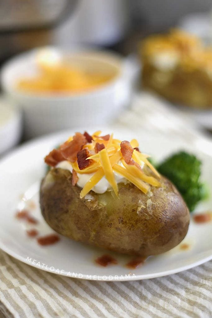 instant pot baked potatoes topped with sour cream cheddar cheese and bacon on a plate with side of broccoli