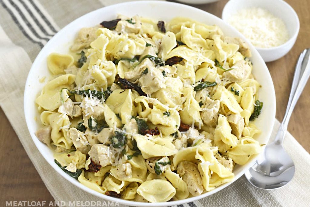 instant pot creamy chicken tortellini pasta in a white bowl with spinach, sun dried tomatoes and parmesan cheese