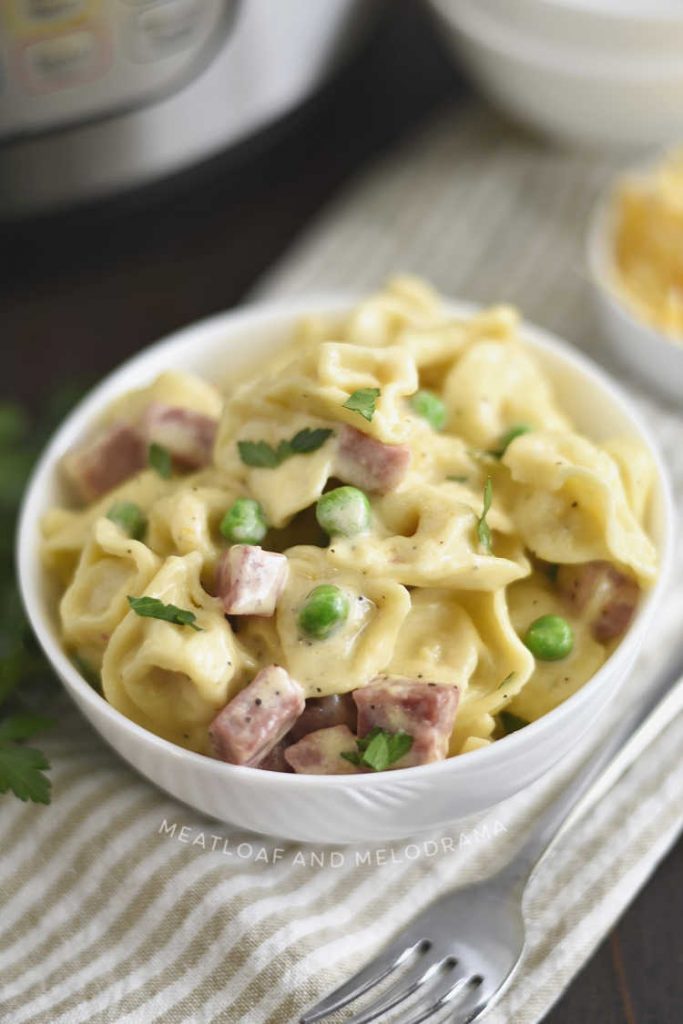 bowl of creamy instant pot ham and cheese tortellini with peas on a napkin with fork