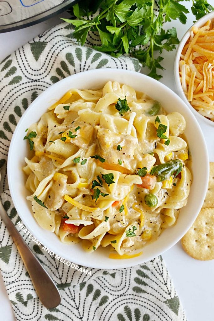 instant pot tuna noodle casserole with frozen peas and carrots in white bowl with cheese and parsley