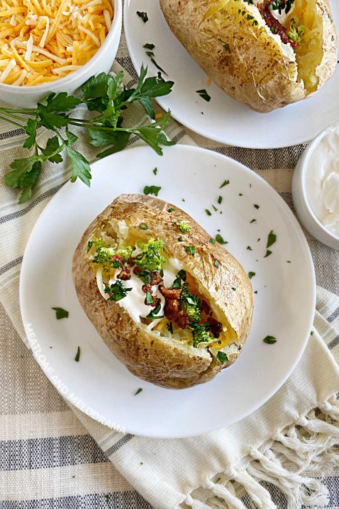 2 baked russet potatoes on white plates with cheese and sour cream