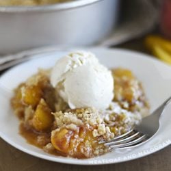 air fryer peach crisp topped with vanilla ice cream on a white plate