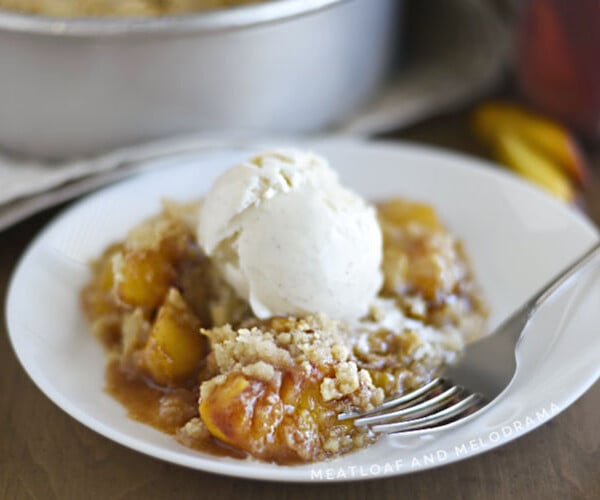 air fryer peach crisp topped with vanilla ice cream on a white plate