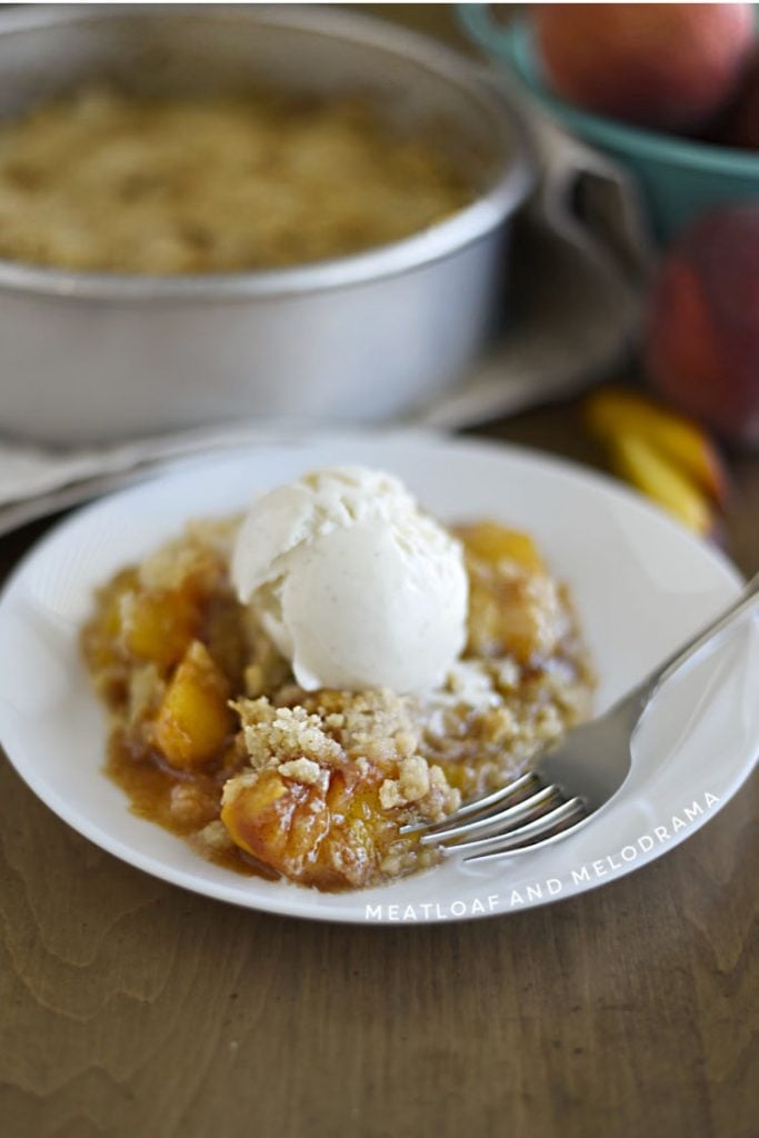 air fryer baked peach crisp on white plate with scoop of vanilla ice creams on