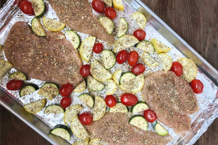 chicken breasts on a baking sheet with sliced zucchini, yellow squash and grape tomatoesu