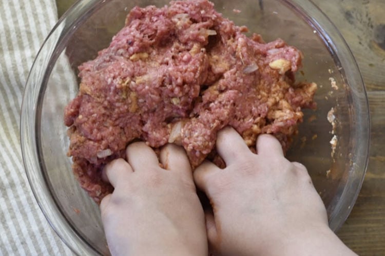 mixing meatloaf ingredients in a glass bowl with hands