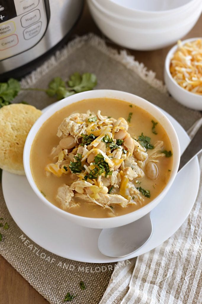 Instant Pot white chicken chili with white beans, corn and cheese in a white bowl with cilantro