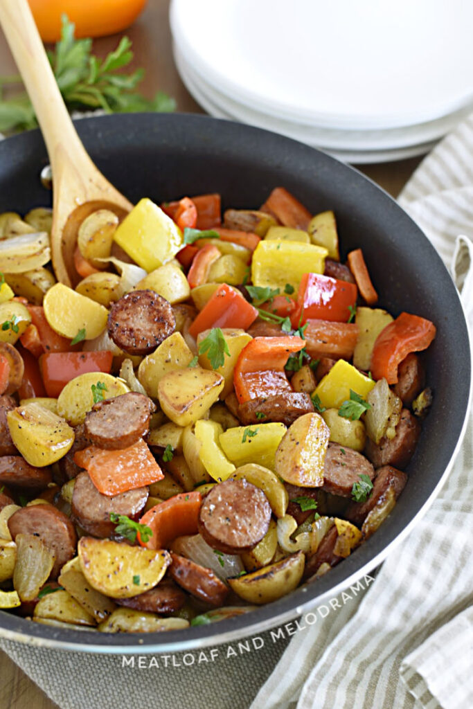 sliced smoked sausage with cut baby potatoes, peppers and onions in a skillet