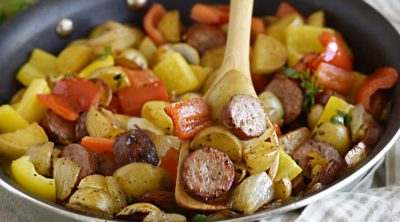 fried kielbasa with potatoes, peppers and onions on wooden spoon in a skillet
